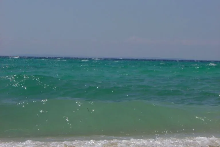 The green-turquoise water off Kalogria with a breaking wave and the Kassandra peninsula on the horizon